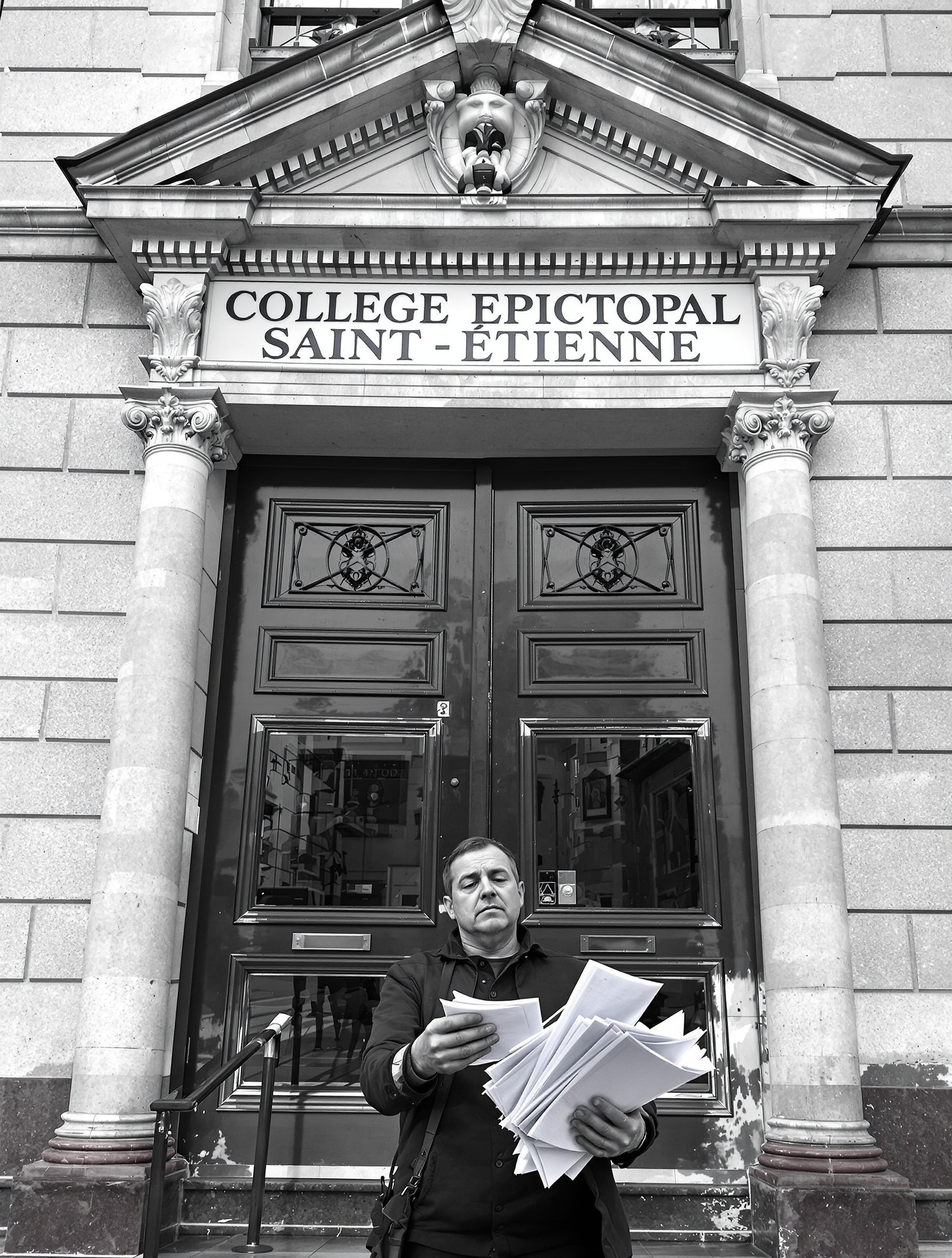 Parent stressé devant le Collège Episcopal Saint-Étienne à Strasbourg, dossier d'inscription en main.